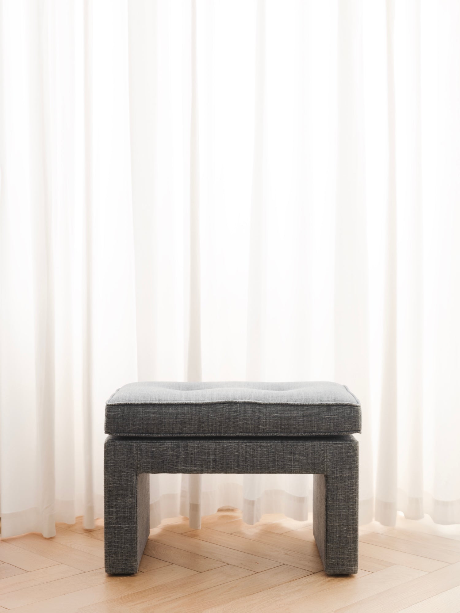 Blue upholstered stool in a room with light-colored curtains