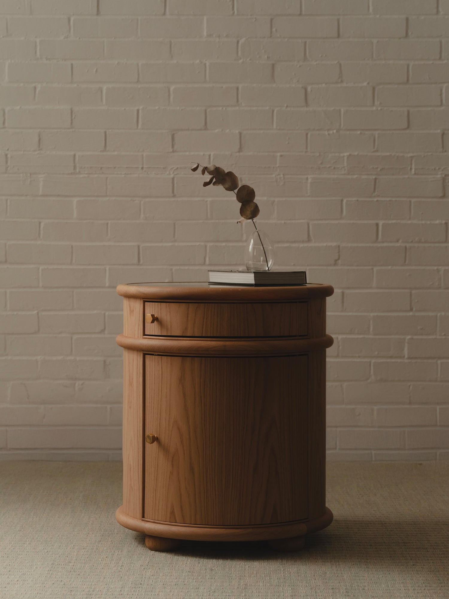 Wooden bedside table with a small plant against a brick wall.