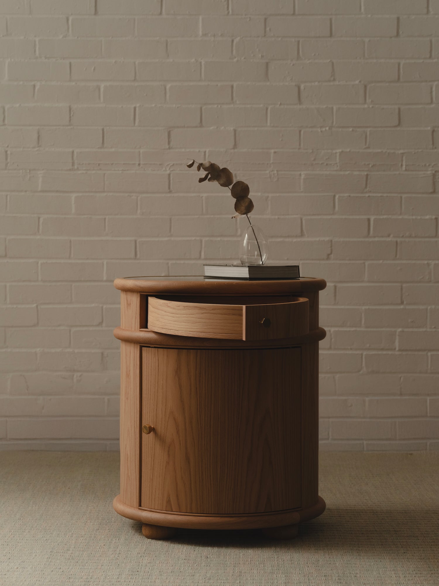 Oak bedside table with brass handles against a brick wall.