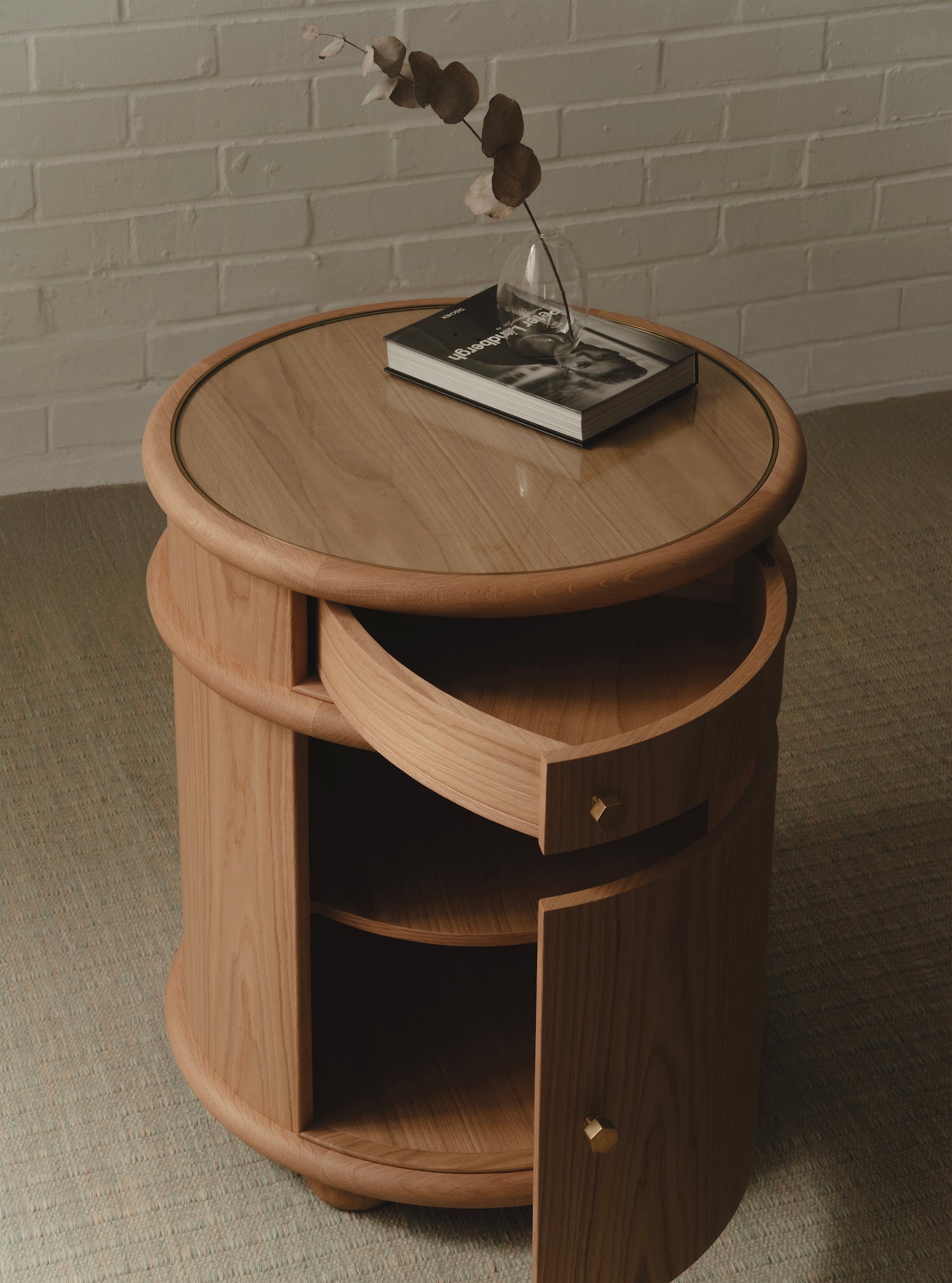 Round wooden bedside table with drawer, a curved door and brass handles.