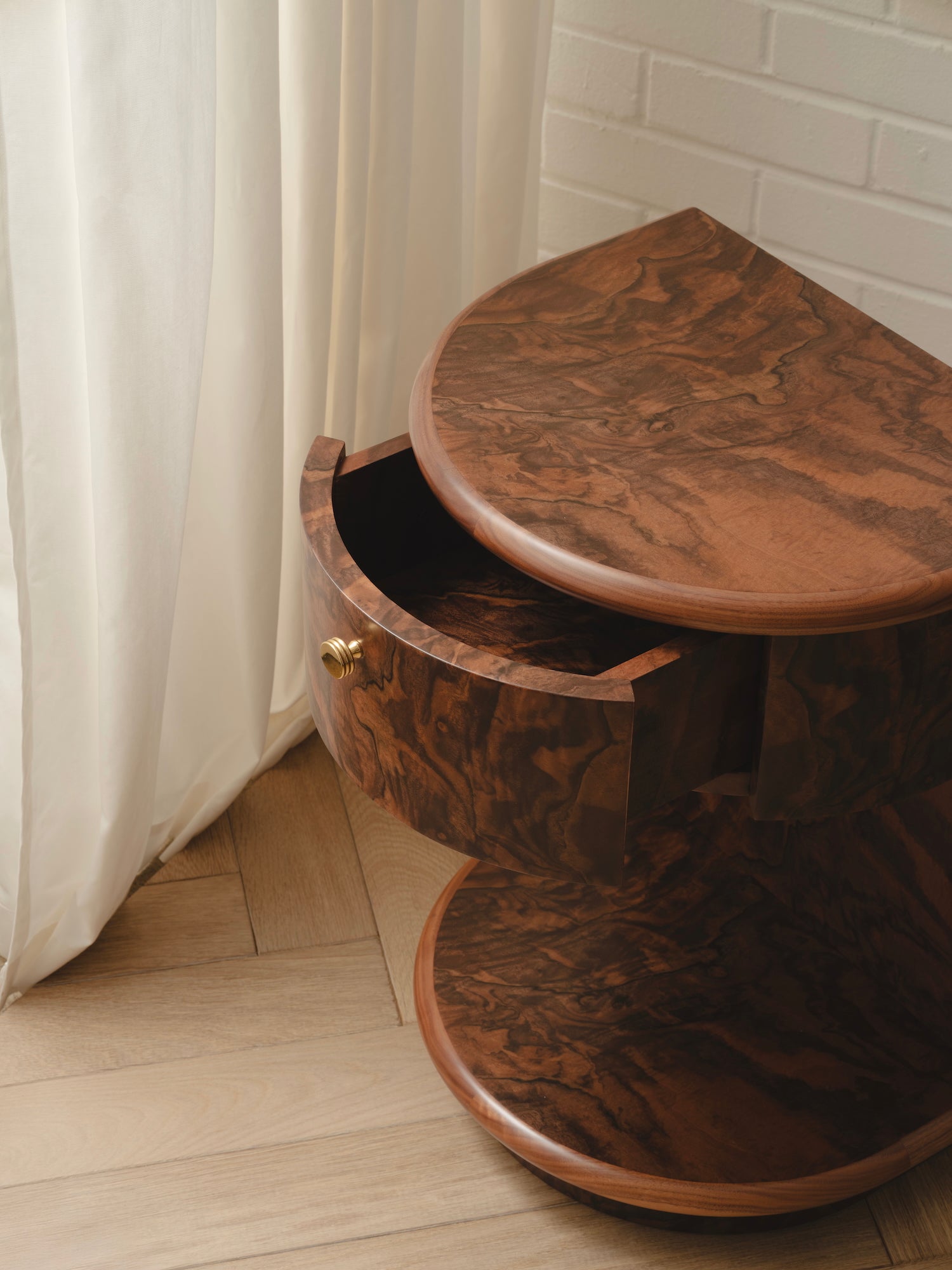 Wooden side table with a curved design in a burr finish with a brass handle.