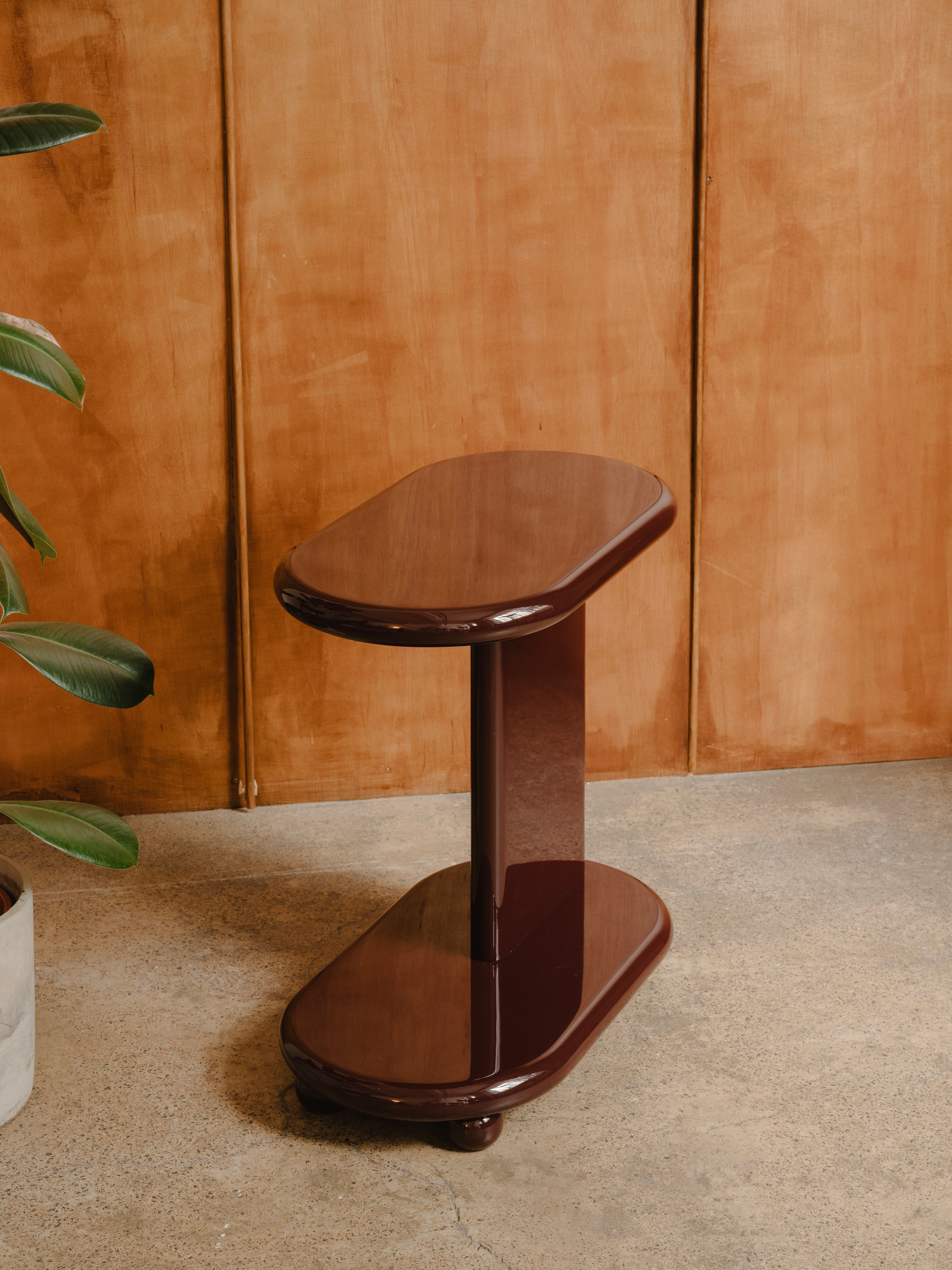 Wooden side table against a wooden panelled wall, in deep red high gloss lacquer finish.