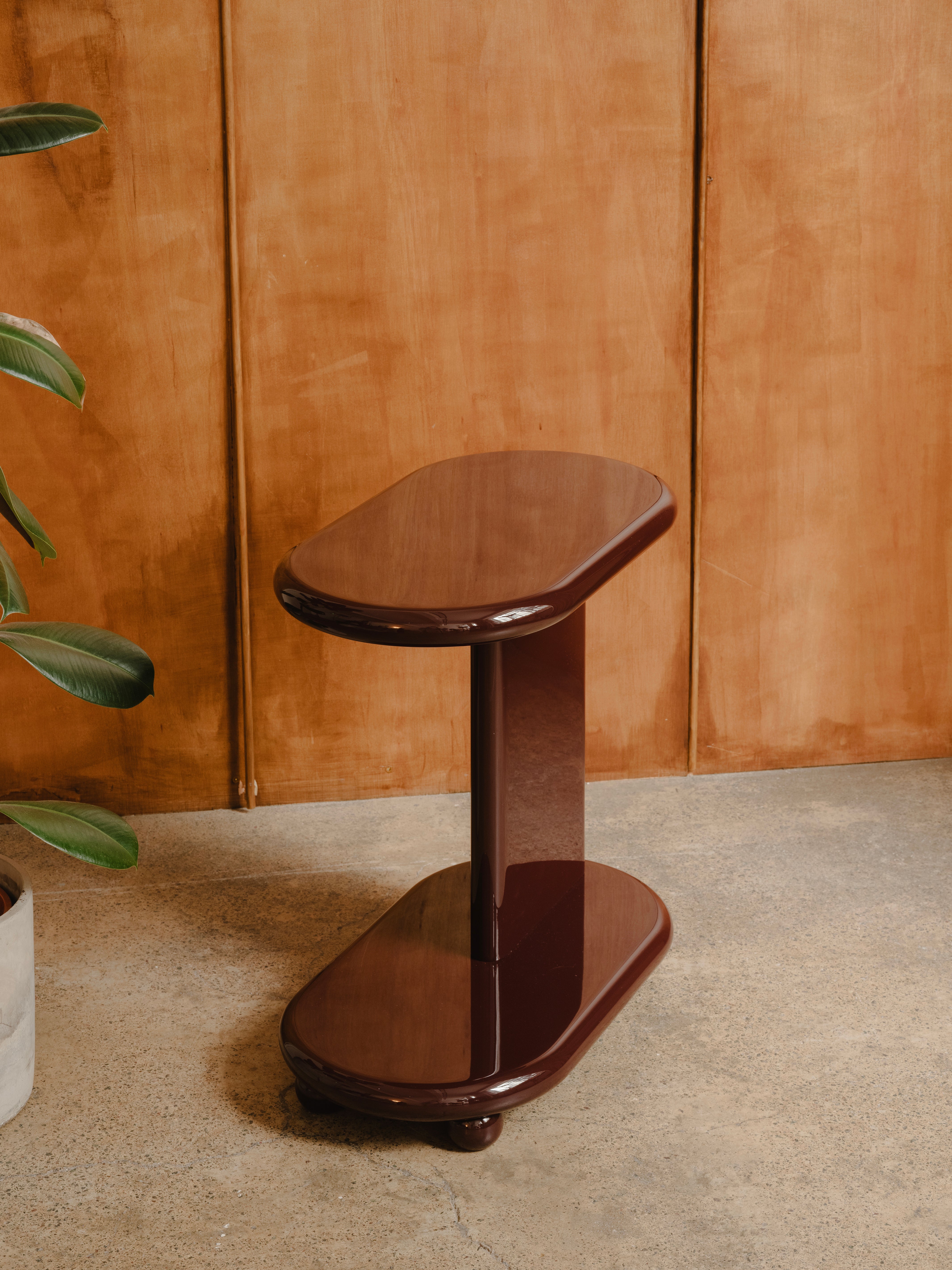 Wooden side table against a wooden panelled wall, in deep red high gloss lacquer finish.