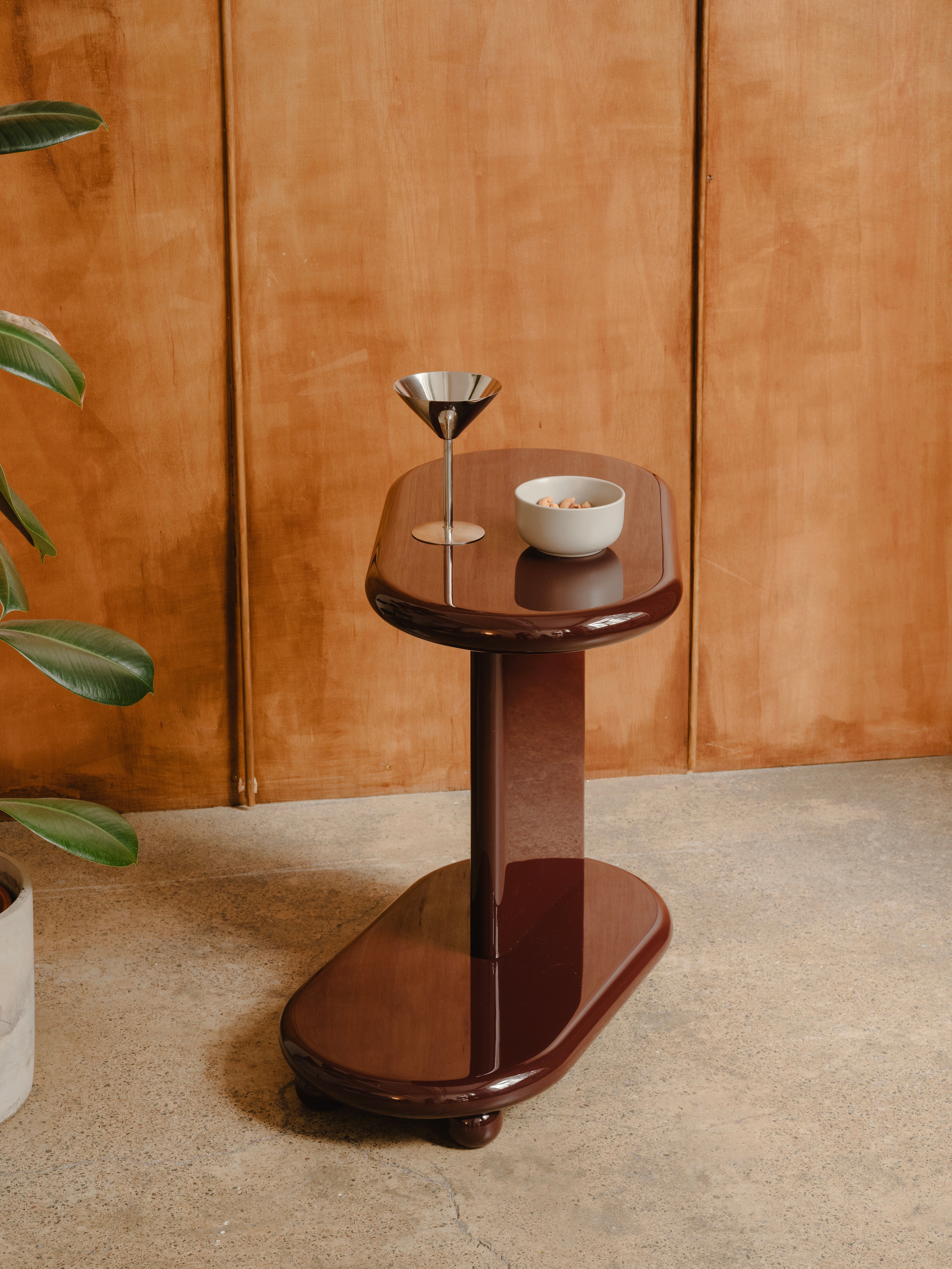 High gloss lacquered side table with a silver martini glass against a wood panelled wall. 