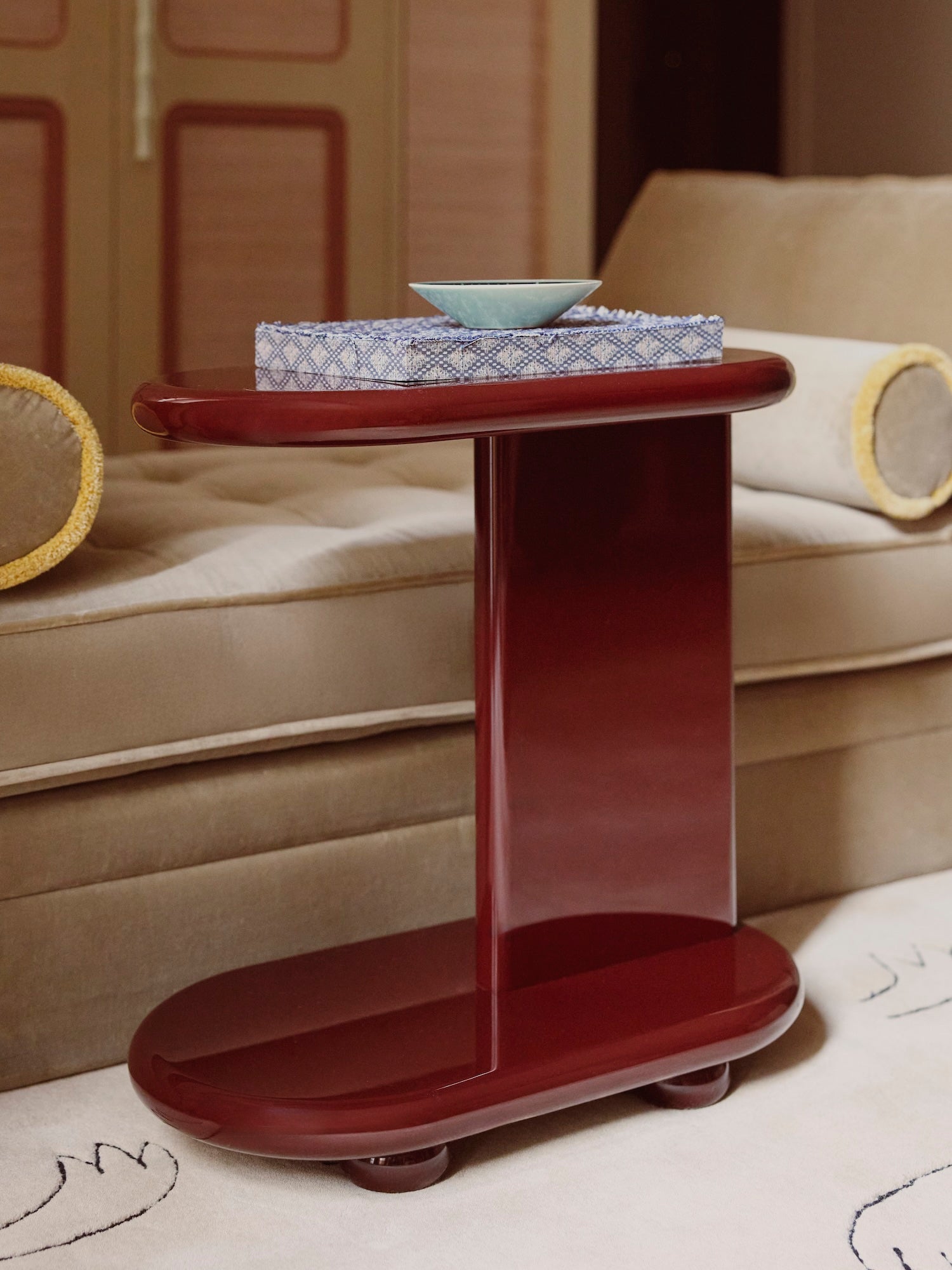 Red high gloss lacquered side table with a bowl on top in a living room setting.