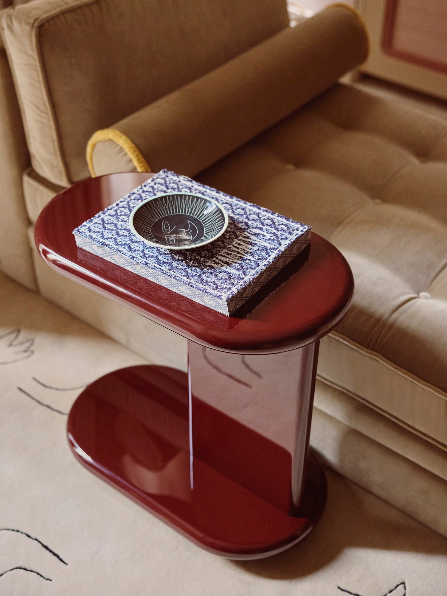 High gloss lacquered side table in a rich red colour, with a decorative bowl on top next to a beige sofa.