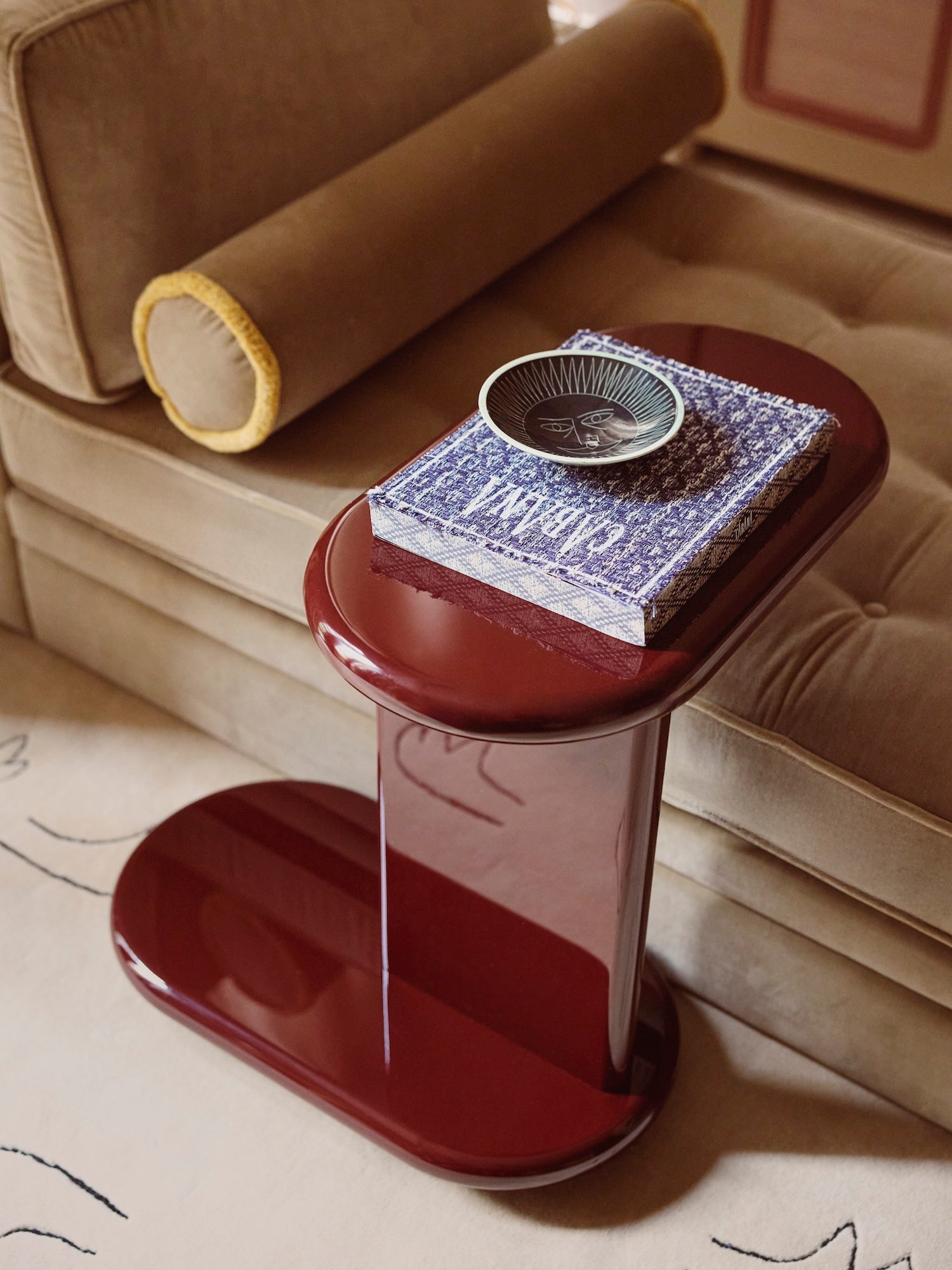 Lacquered side table with swivel top in a rich glossy red colour, next to a caramel brown sofa. 